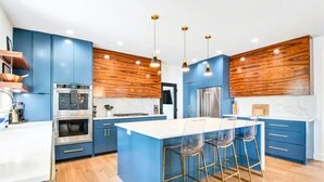 Una cocina moderna con armarios azules, una isla central con taburetes de bar, electrodomésticos de acero inoxidable y paneles de madera.