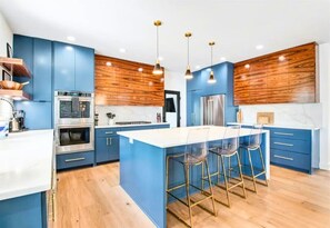 Una cocina moderna con armarios azules, una isla central con taburetes de bar, electrodomésticos de acero inoxidable y paneles de madera.