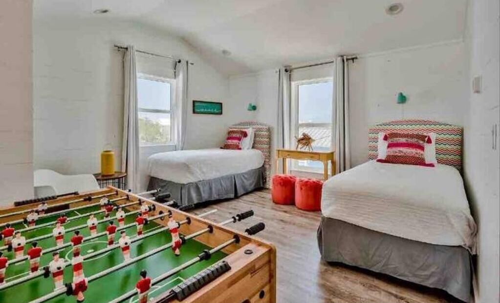 Una habitación con dos camas, una mesa de futbolín y una ventana.