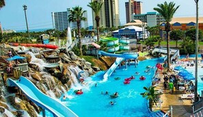 A water park with multiple slides and pools, surrounded by palm trees and buildings. - Luxury Beach Oasis~Sleeps 26! FREE Golf Cart~Pool/HotTub~Game Room (Destin)