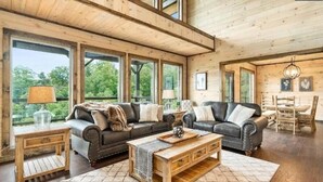 Un salon spacieux doté de grandes fenêtres, d’un plafond en bois et d’un coin salon confortable avec un canapé et un fauteuil.