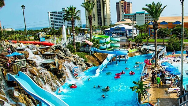 A water park with multiple slides and water features, surrounded by palm trees and buildings.