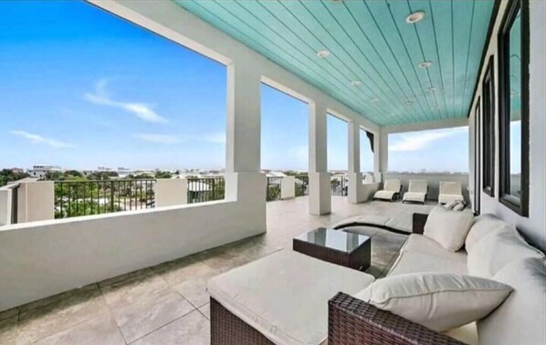 A spacious balcony with a view of the city skyline, featuring a seating area with cushions and a coffee table.