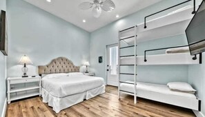 A bedroom with a large bed, a bunk bed, wooden flooring, and a ceiling fan.