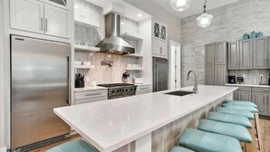 A modern kitchen with a large island, stainless steel appliances, and light blue bar stools.