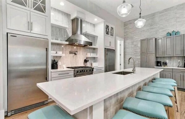 Una cocina moderna con una isla grande, electrodomésticos de acero inoxidable y taburetes de color azul claro.