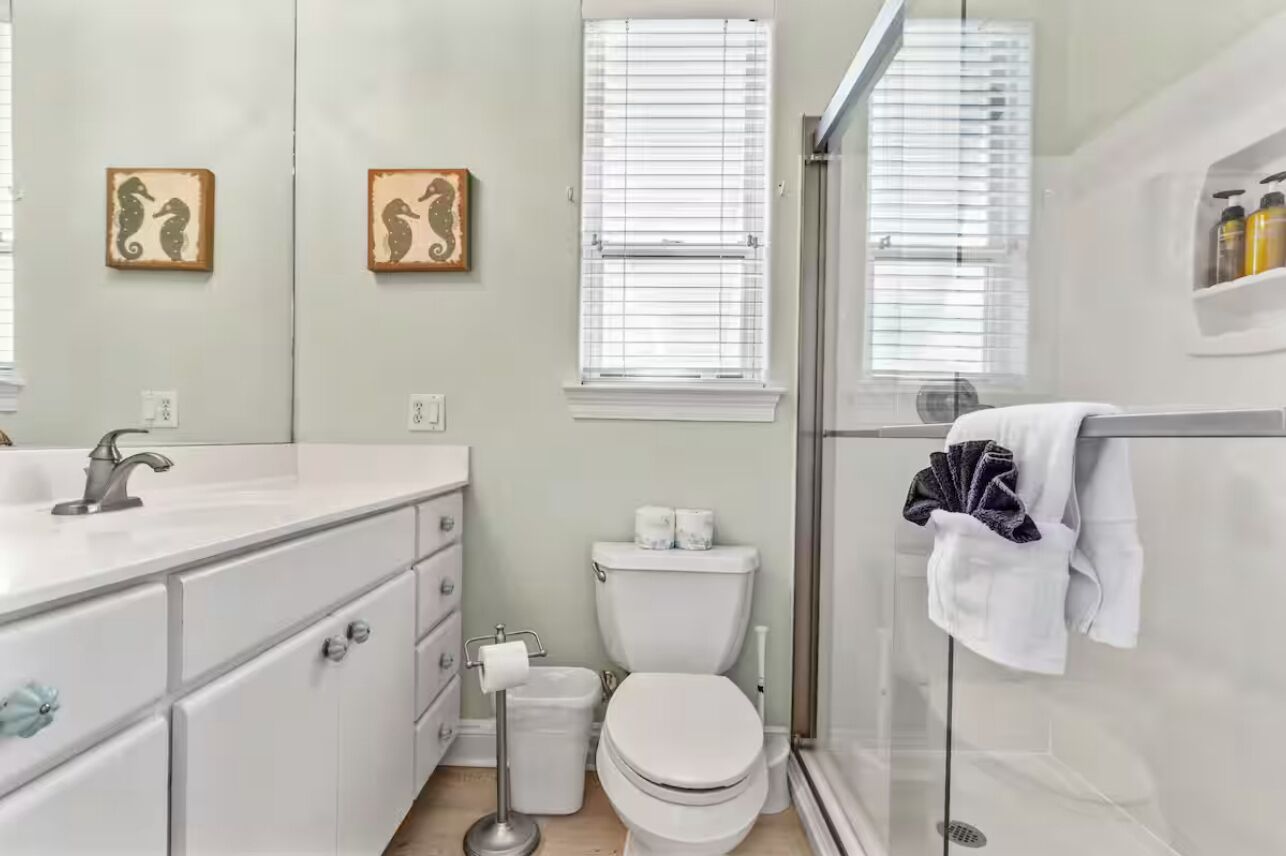 A modern bathroom with a white sink, toilet, and shower. There are two framed pictures on the wall and a towel rack with a towel.