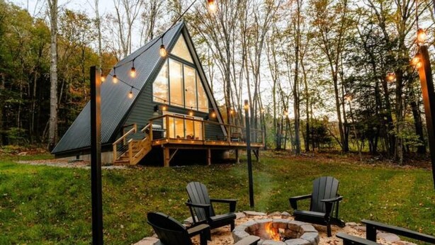 Une cabane avec un toit triangulaire, une terrasse et un foyer avec des chaises.