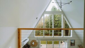 Une chambre de style loft moderne, avec un plafond en pente, de grandes fenêtres et une vue sur une zone boisée.