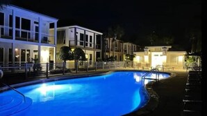 A nighttime view of a hotel with a swimming pool, multiple buildings, and outdoor seating areas. - Waterfront Villa-Pool-King Bed-Steps to the Sand! (Destin)