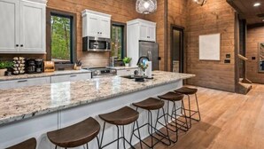A modern kitchen with granite countertops, white cabinetry, stainless steel appliances, and bar stools.
