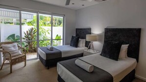 A hotel room with two beds, a ceiling fan, a large window with a view of greenery, and a wicker chair. - Port Douglas Mirage Villa#423 (Port Douglas)
