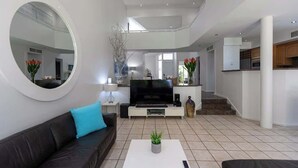 A modern living room with a black leather sofa, a white coffee table with a plant, and a large flat-screen TV. - Port Douglas Mirage Villa#423 (Port Douglas)