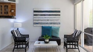 A modern living room with a sofa, two chairs, a coffee table, and a large abstract painting. - Port Douglas Mirage Villa#423 (Port Douglas)