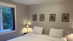 Une chambre à coucher comprenant un lit, une table de chevet, une lampe et quatre reproductions botaniques encadrées accrochées au mur.