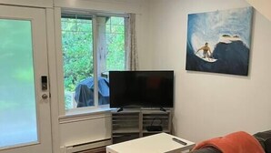A living room with a TV, a sofa, a coffee table, and a painting on the wall. - Sienna's Tree House #3 (Tofino)