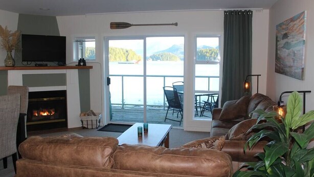 Una sala de estar con chimenea, sofás de cuero, televisor y vista a un lago.