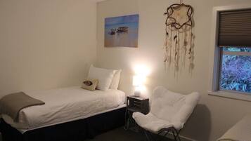 A bedroom with a bed, bedside table, chair, and a dreamcatcher decoration.