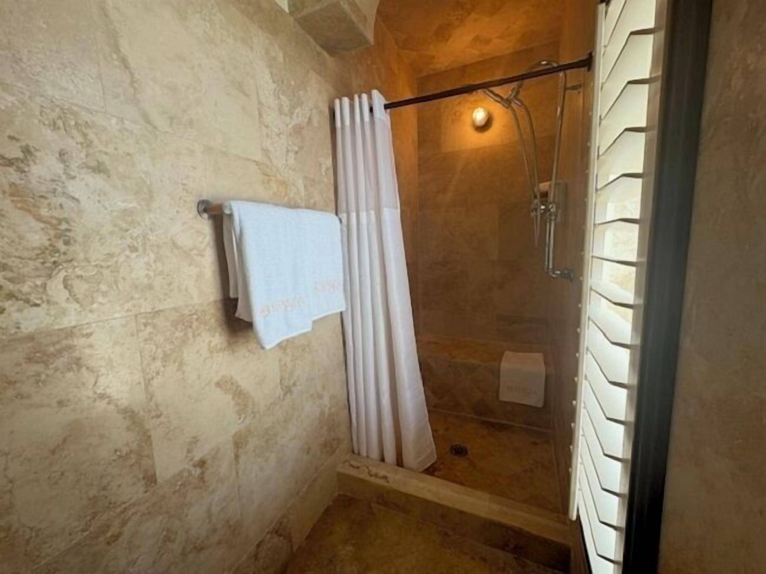Una ducha con puerta de vidrio, un perchero con una toalla y un cabezal de ducha.