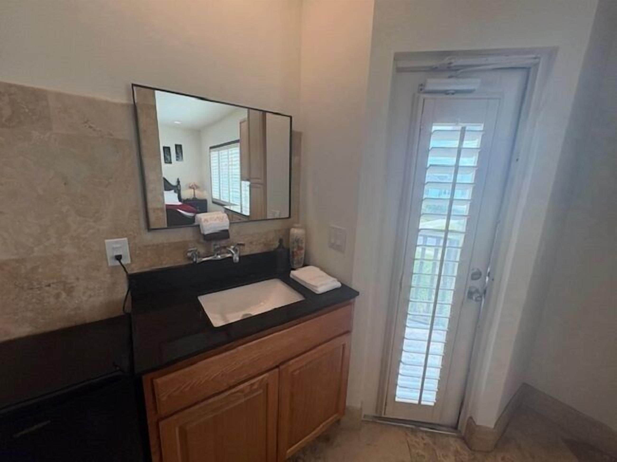 Une salle de bain avec un comptoir noir, un lavabo, un miroir et des armoires en bois.