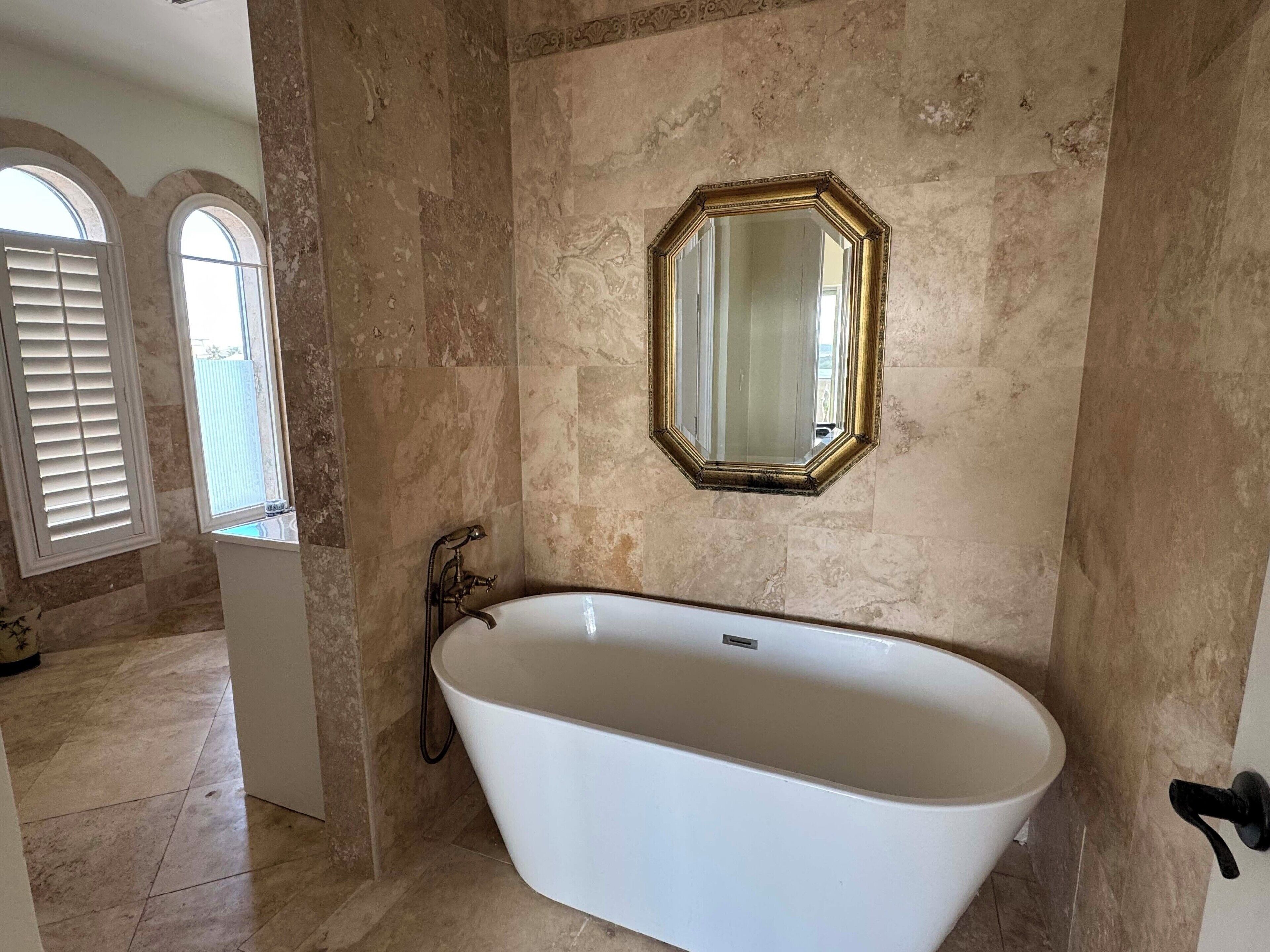 Ein Badezimmer mit einer freistehenden Badewanne, einem großen Spiegel und einem Fenster mit Rollläden.
