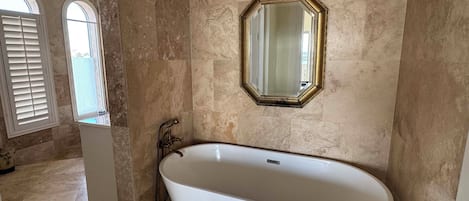 A bathroom with a freestanding bathtub, a large mirror, and a window with shutters.