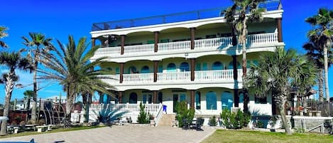Um hotel com vários andares, um pátio central, palmeiras e uma piscina.
