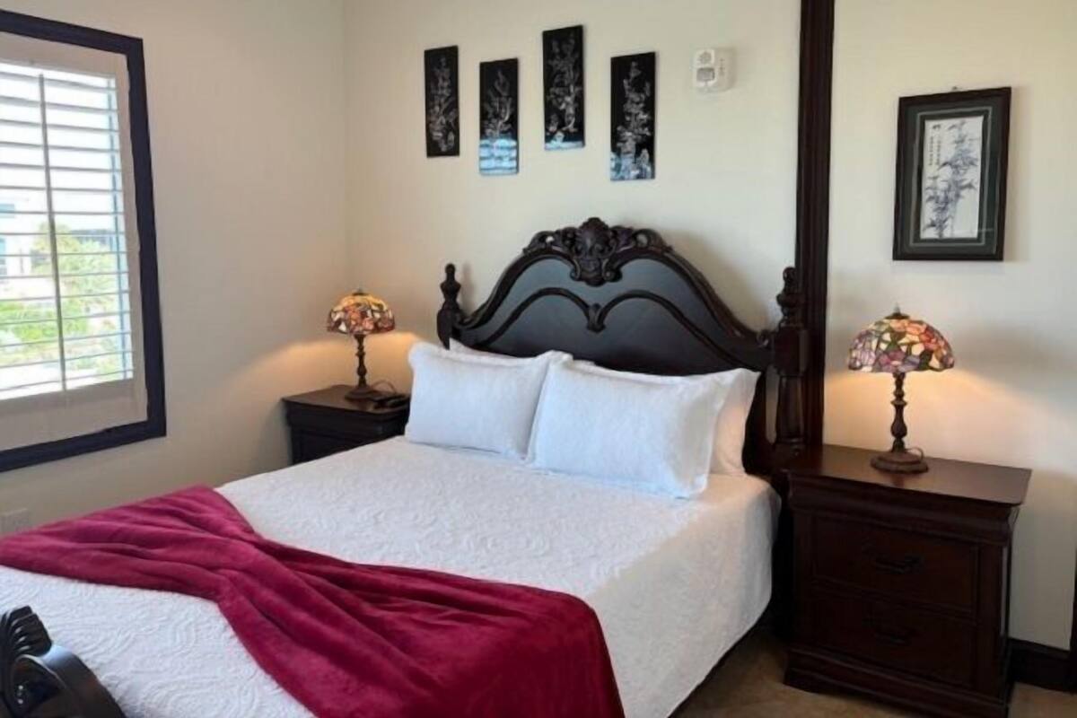 A neatly made bed with a white comforter and a red blanket, flanked by two nightstands with lamps.