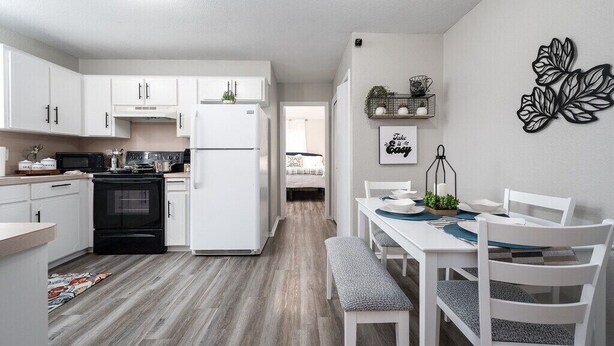 A modern kitchen with white cabinets, a black stove, and a refrigerator. There is a dining area with a white table and chairs. - Cozy 3-bedroom Townhome in Charming Killeen With WiFi, AC (Killeen)