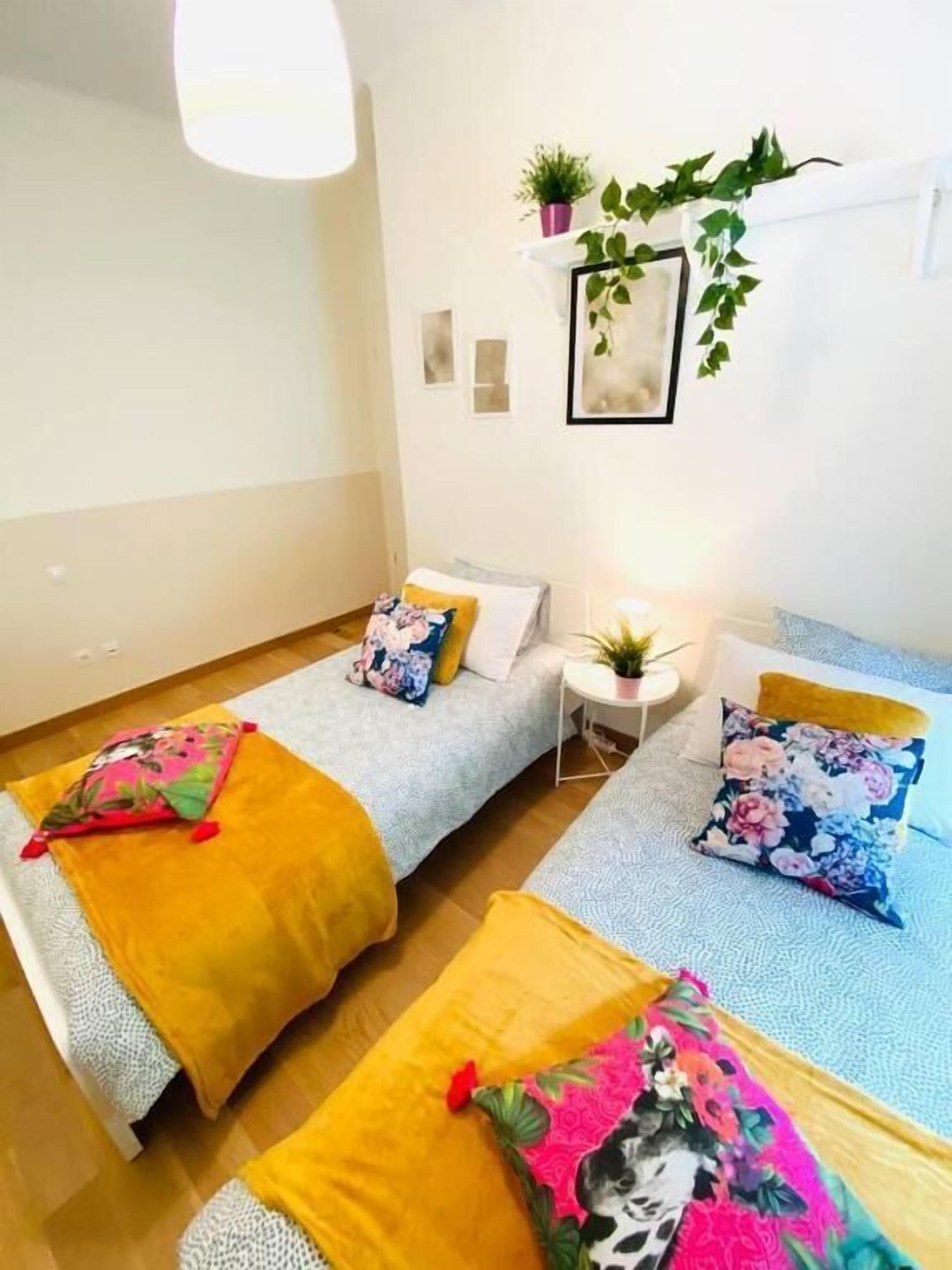 A small, well-lit room with two beds, each with colorful bedding and a small side table.
