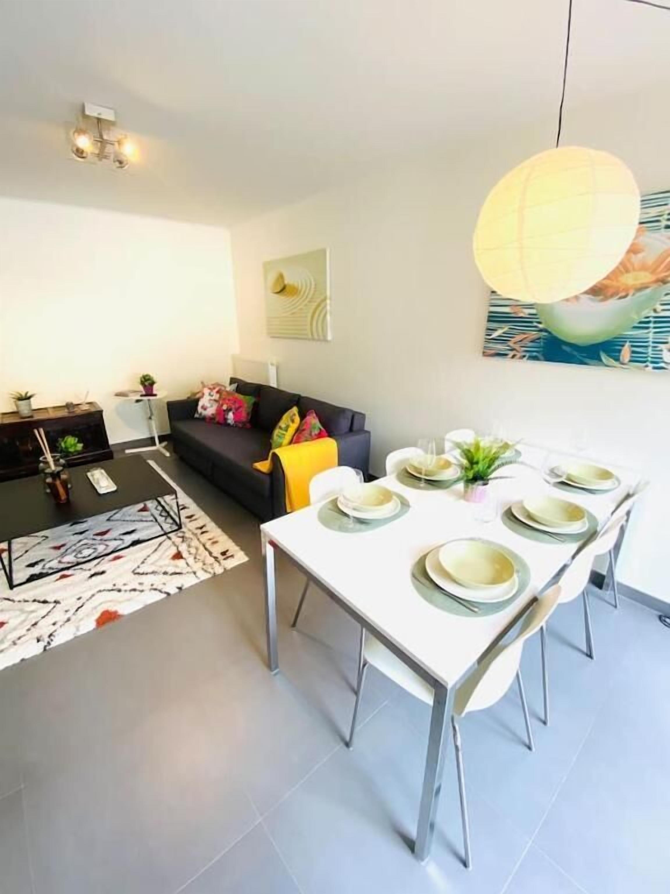 A modern living room with a dining area, featuring a sofa, a coffee table, and a dining table set for six.