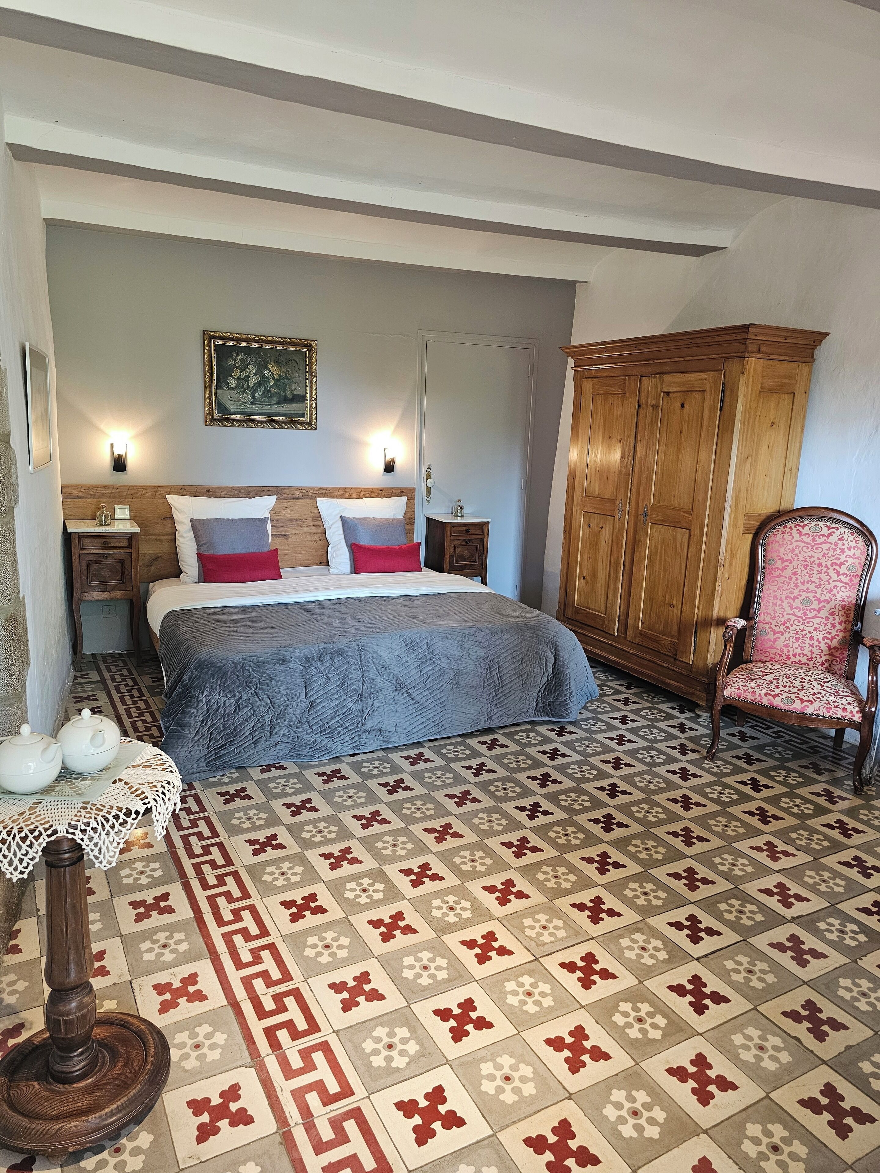 Une chambre à coucher comprenant un lit, une armoire en bois, une chaise, une table de chevet et une lampe murale décorative.