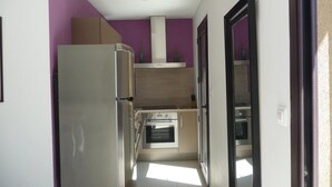 A narrow kitchen with a refrigerator, oven, and cabinets, and a purple wall. - Apartment 'Luna Verde' with Shared Pool, Private Terrace and Wi-Fi (Porto-Vecchio)