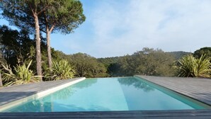 A rectangular swimming pool with a wooden deck in the foreground, surrounded by trees and a hilly landscape in the background. - Apartment 'Luna Verde' with Shared Pool, Private Terrace and Wi-Fi (Porto-Vecchio)