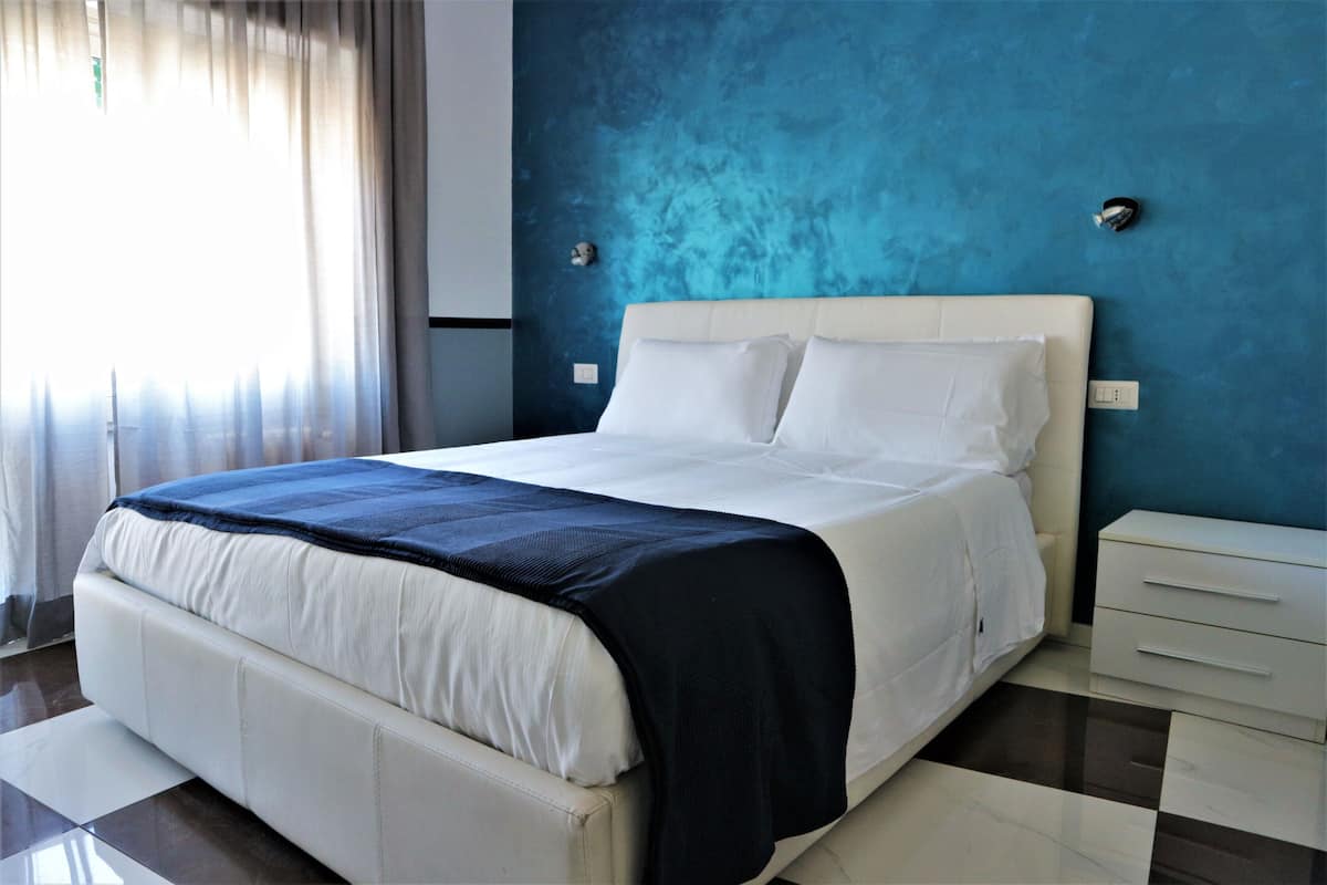 A modern bedroom with a large bed, a nightstand, and a blue accent wall.