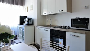 A modern kitchen with white cabinets, a gas stove, a microwave, and a refrigerator. - Luxury Vatican Rooms (Rome)