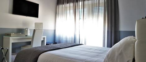 Una habitación de hotel moderna con cama, escritorio, silla, televisor de pantalla plana y un amplio ventanal con cortinas.