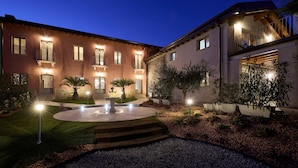Un patio bien iluminado con una fuente, escaleras que llevan a una puerta y un edificio con balcones y ventanas.