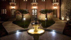 Un patio con una fuente en el centro, muros de piedra y un edificio con varias ventanas y balcones.