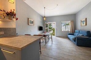 A modern kitchen with a dining area, a blue sofa, and a TV.