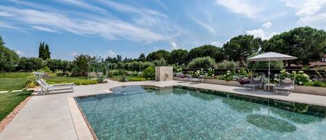 A clear swimming pool with lounge chairs and a garden area.
