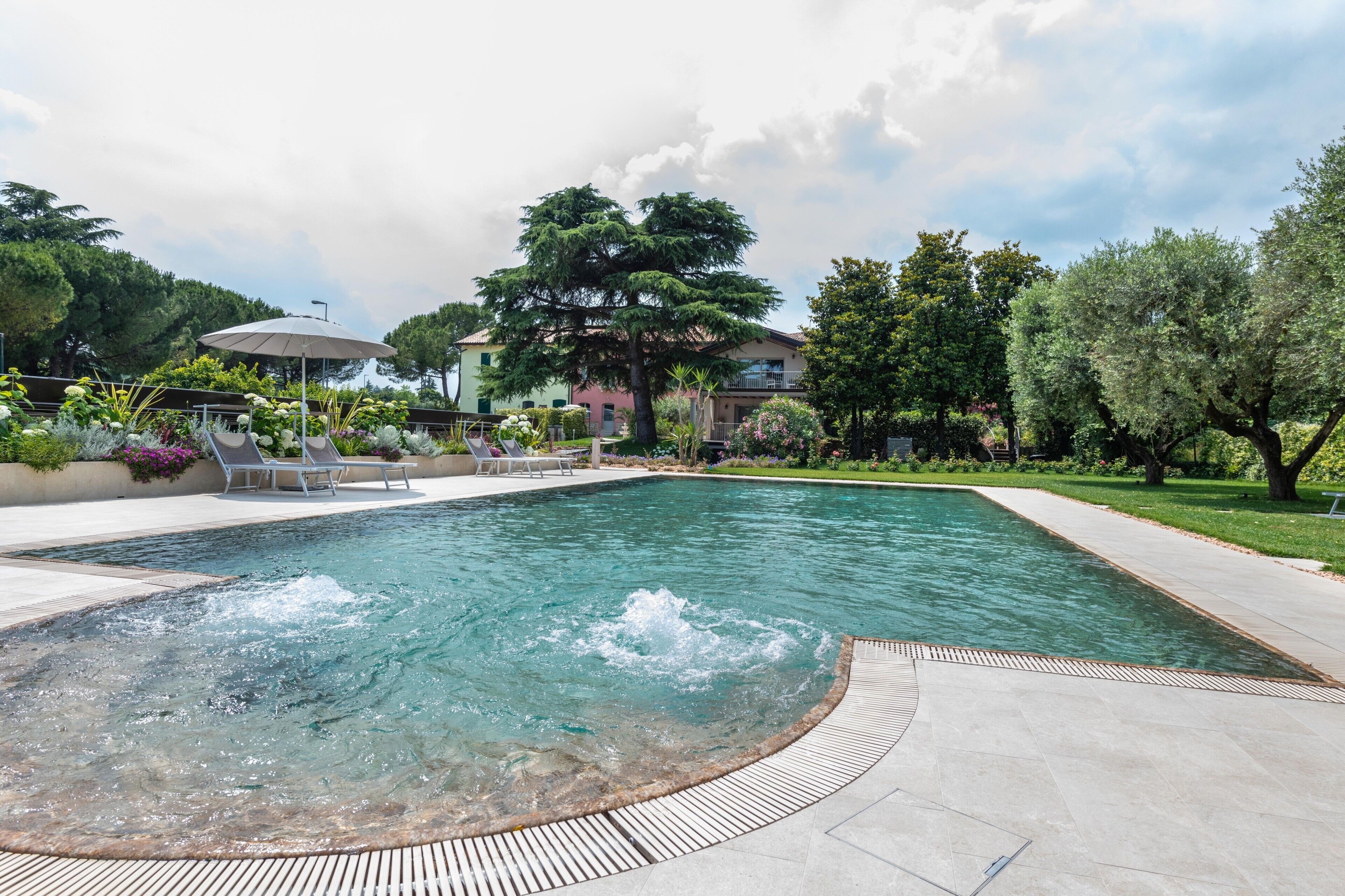 Une piscine avec un jacuzzi, entourée de chaises longues et de verdure.