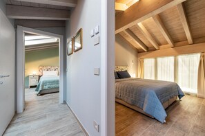 Een slaapkamer met een bed, houten balken, een nachtkastje en een raam met gordijnen.
