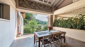 A balcony with a wooden table and chairs, a view of greenery, and a patterned ceiling. - Apartment 'Abaye 6 Cabernet - Charm' with Shared Pool, Wi-Fi and Air Conditioning (Soiano del Lago)