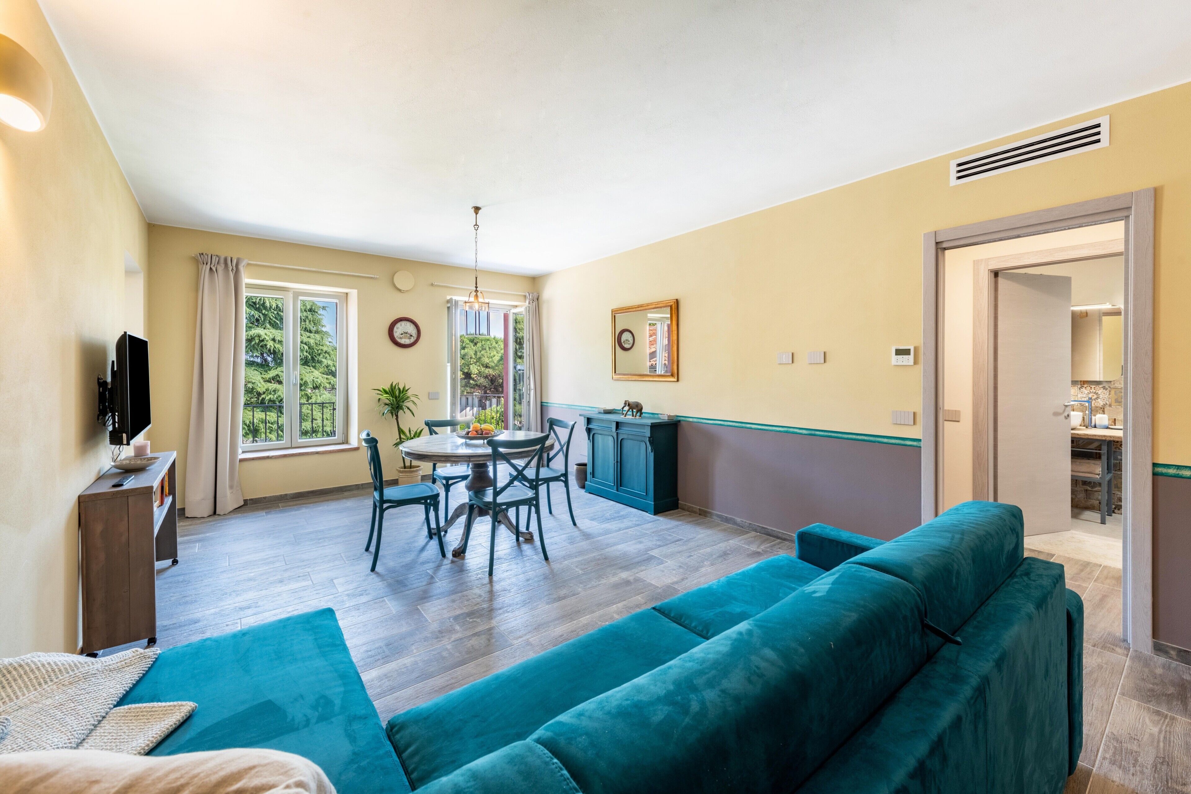 Una habitación con un sofá color turquesa, una mesa de comedor con sillas, un televisor y una ventana con cortinas.