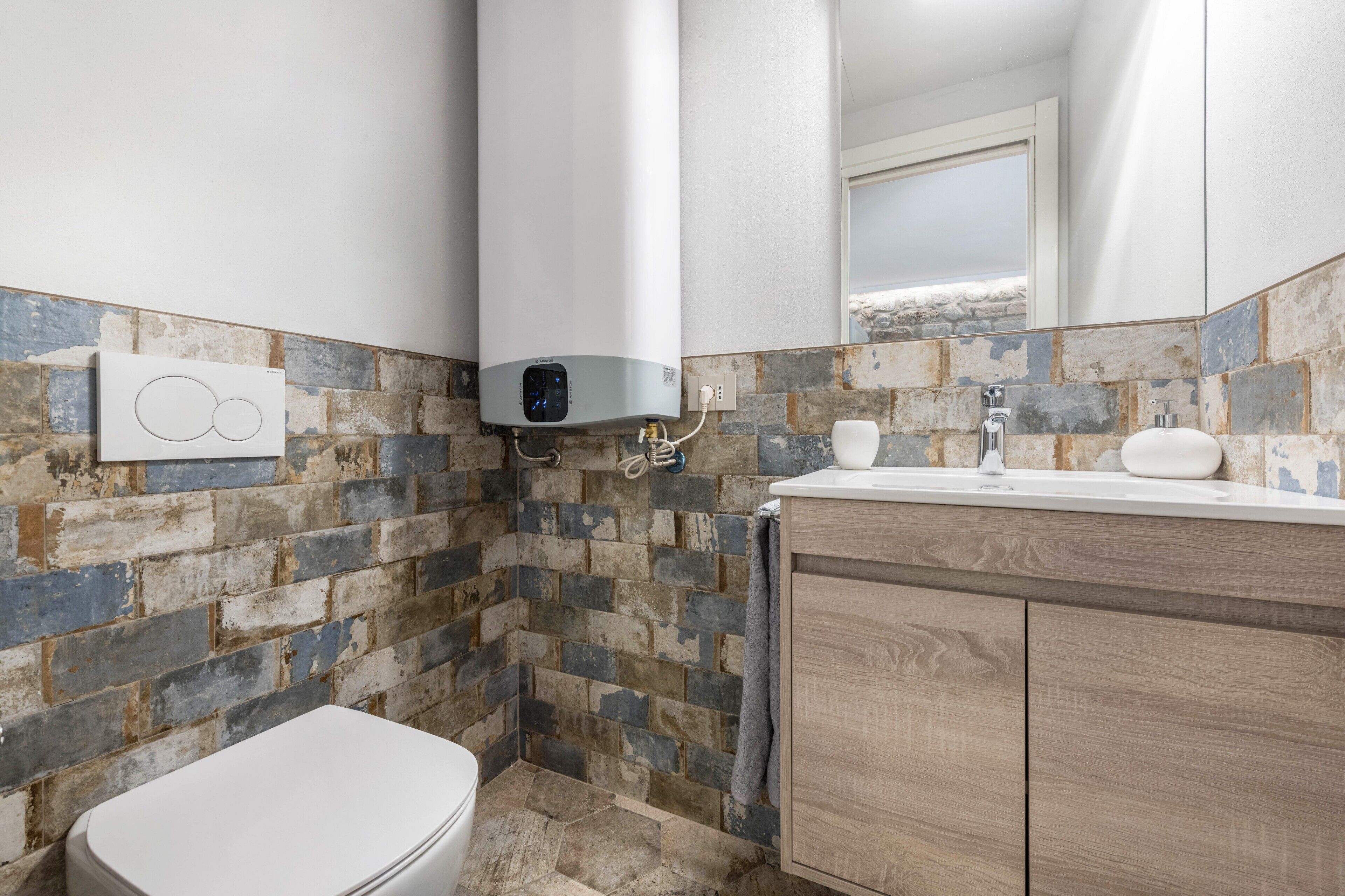 Un baño con inodoro blanco, zona de ducha, pared con revestimiento de ladrillo y tocador de madera con lavabo.