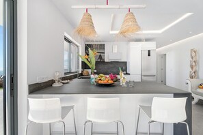 Une cuisine moderne avec un îlot central, des tabourets de bar blancs et des luminaires suspendus.