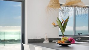 Een moderne keuken met een groot raam met uitzicht op de oceaan, een schaal met fruit en een decoratieve glazen koepel.
