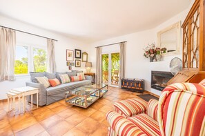 Ein Wohnzimmer mit einer Couch, einem gestreiften Sessel, einem Glastisch, einem Kamin und Blick durch eine Glasdoor.
