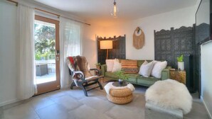 Uma sala de estar com um sofá verde, uma cadeira de madeira, uma luminária e um painel decorativo na parede.
